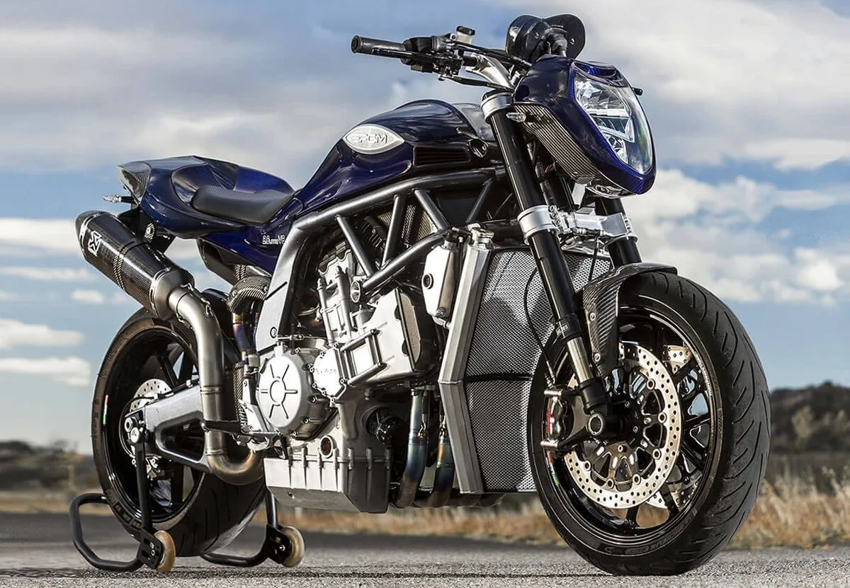 Une moto PGM V8 garée avec une béquille arrière sur une route, un ciel bleu avec des nuages.