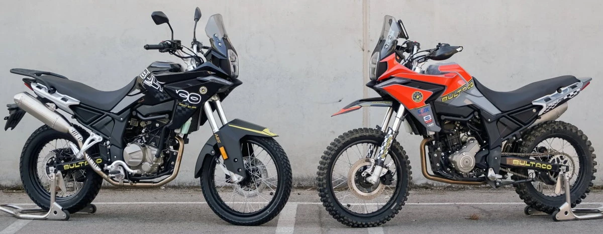Une moto Bultaco Rally GT 300 noire et sa version racing en rouge devant un mur de béton gris.