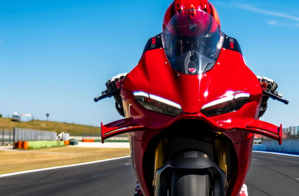 L'avant d'une Ducati 11000 Panigale V4 S rouge de 2027, un ciel bleu et les bords de la piste d'un circuit.
