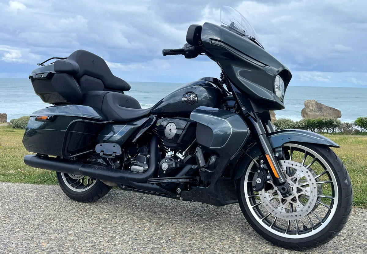 Una moto Harley-Davidson Street Glide Limited negra, vegetación, el océano y un cielo nublado.