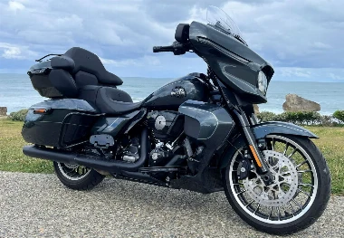 Une moto Harley-Davidson Street Glide Limited noire, de la verdure, l'océan, et un ciel nuageux.