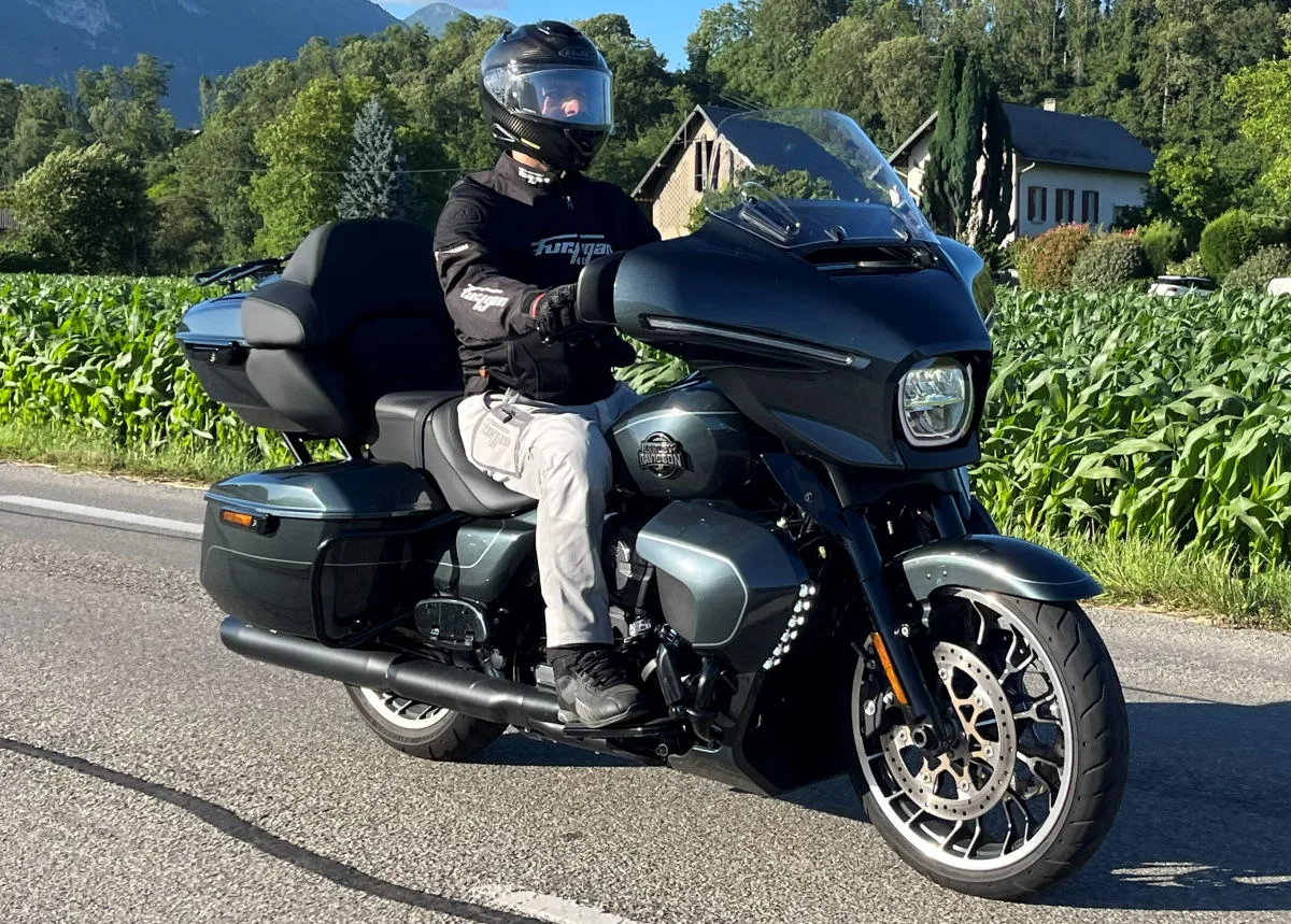 Une moto Harley-Davidson Street Glide Limited sur une route, des plants de maïs, une maison et de la forêt