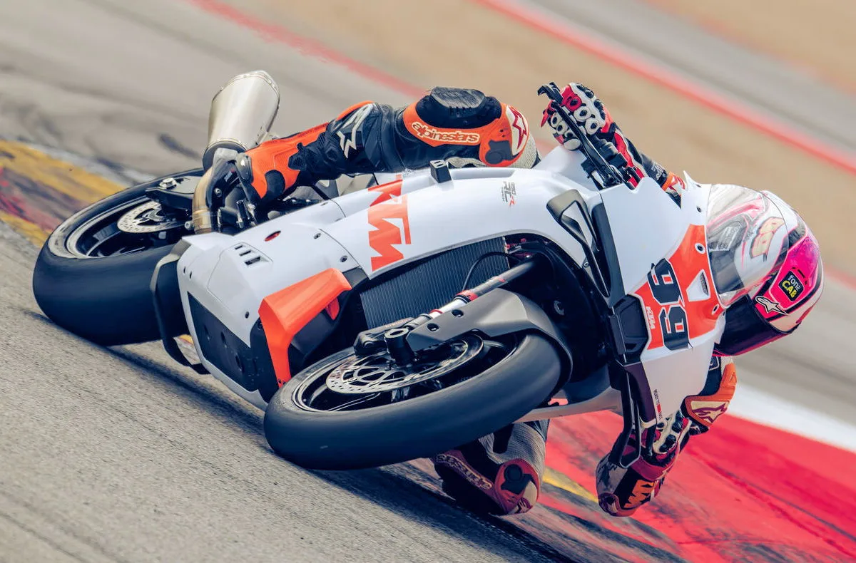 Une moto KTM 990 RC R Track blanche et orange sur un circuit et un casque blanc et rose