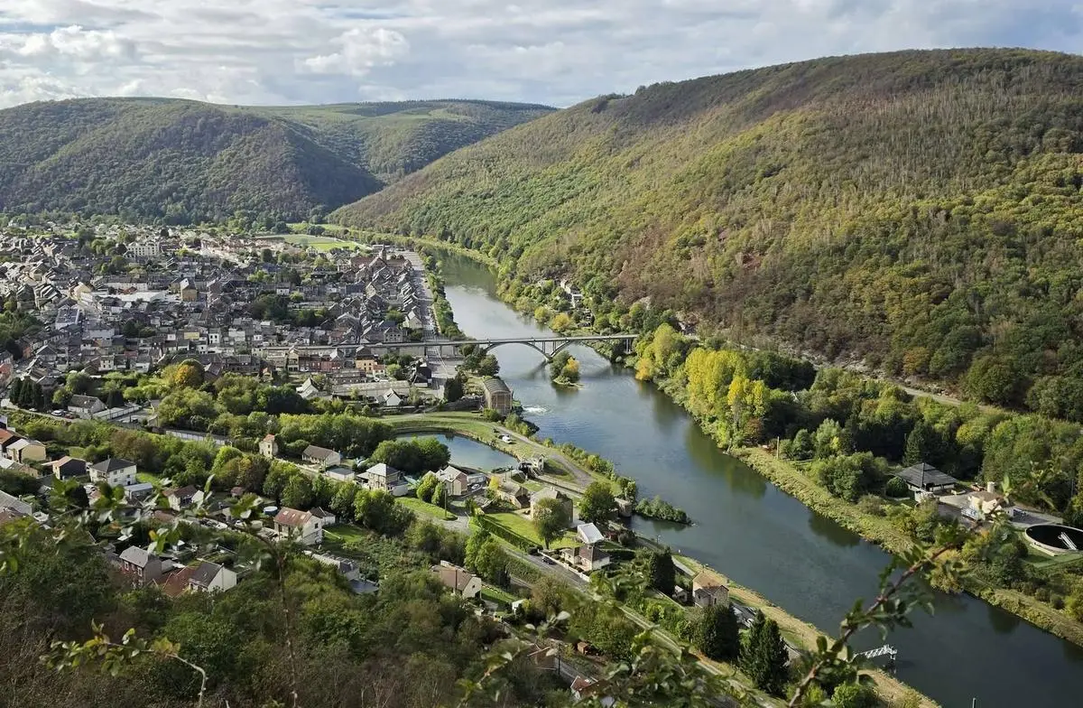 Une vue aérienne sur un fleuve dans une vallée boisée, un pont et un village.