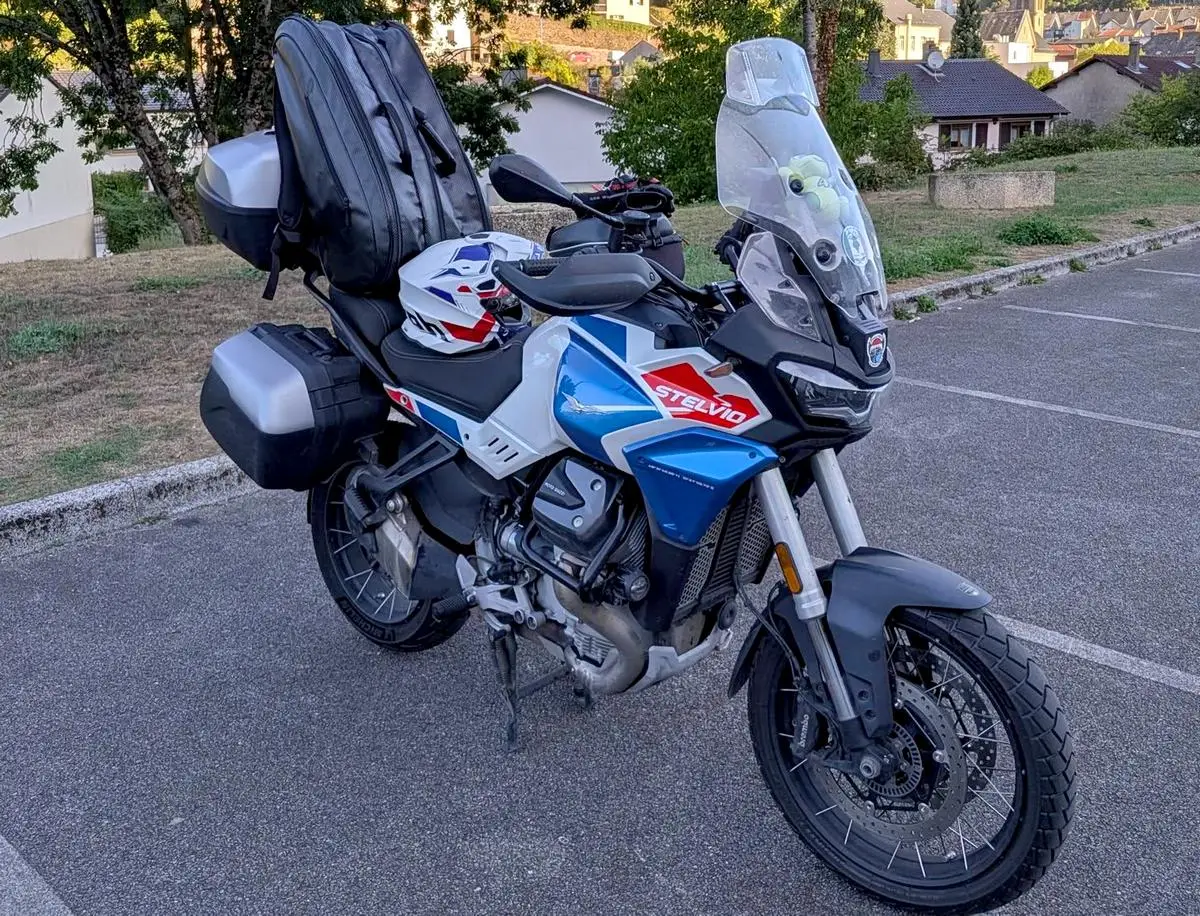 Une moto-guzzi 1000 Stelvio bleu blanche rouge, des valises, un top-case et un sac à dos.