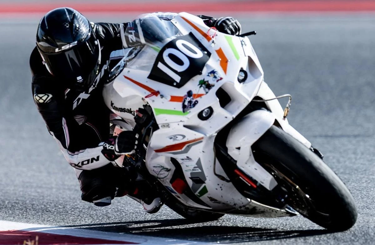Une Kawasaki ZX-10R blanche avec le numéro 100 et une pilote en combinaison noire et blanche