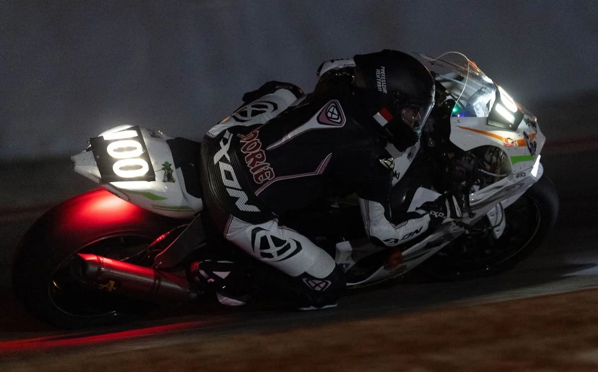 Une Kawasaki ZX-10R blanche avec le numéro 100 et une pilote en combinaison noire et blanche dans la nuit