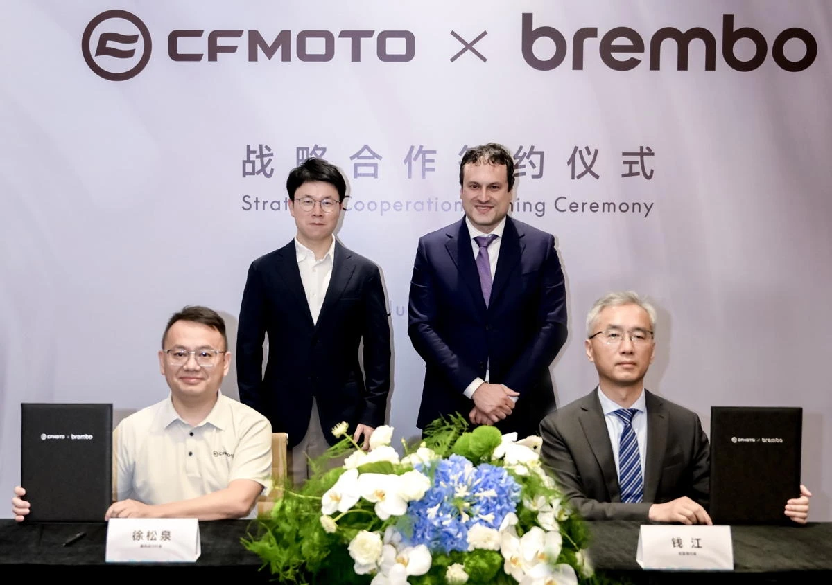 4 personnes en costume pour signer l'accord entre CFMOTO et Brembo, des fleurs sur une table