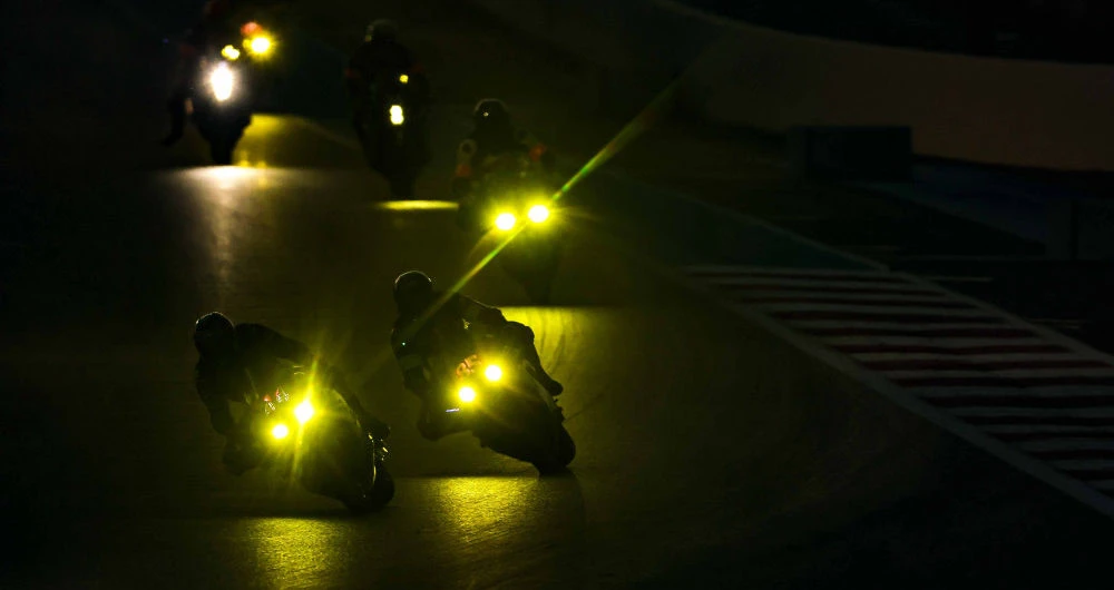 Les phares de plusieurs motos roulant de nuit sur un circuit
