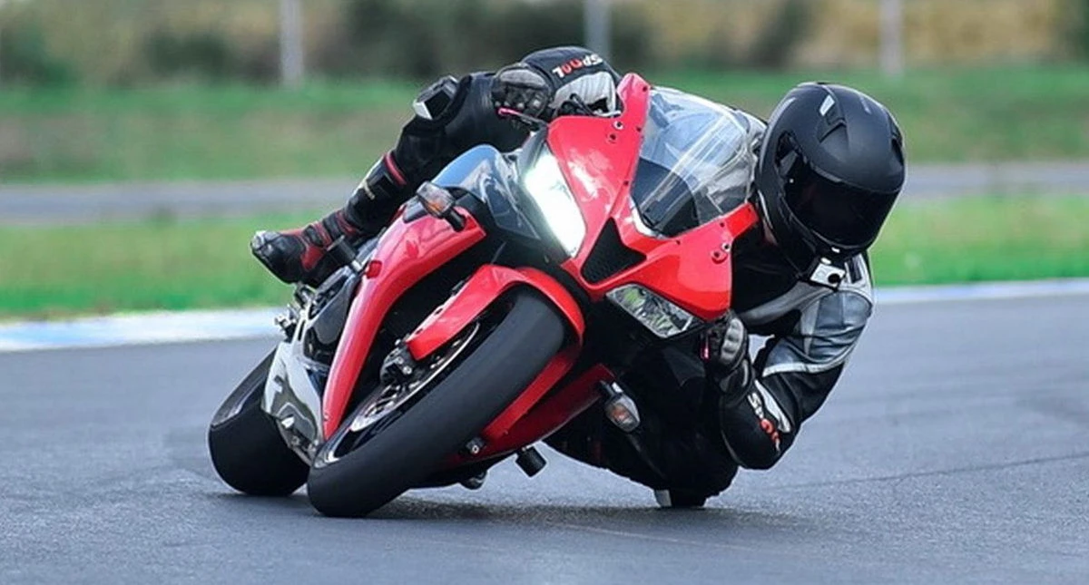 Une moto Honda CBR 600 RR rouge sur circuit et un pilote avec une combinaison noire et un casque noir et le slider de genou frottant l'asphalte.