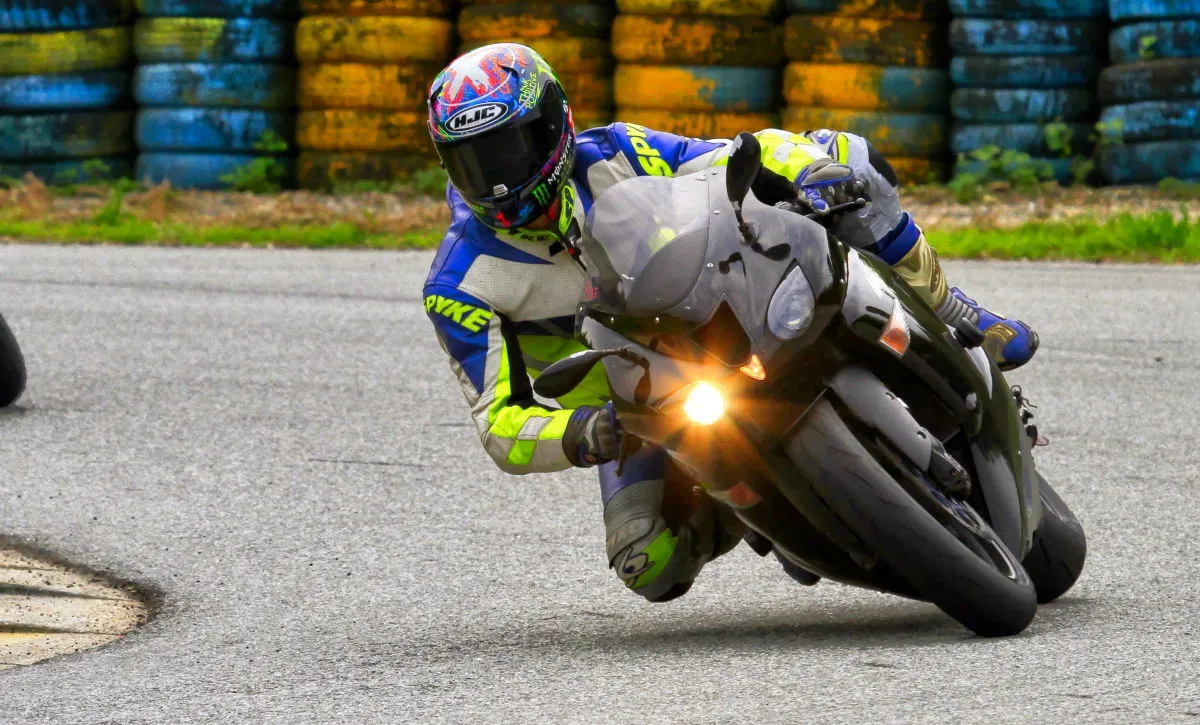 Une Kawasaki ZX-6R noire sur circuit et un pilote habillé en bleu, jaune et blanc.