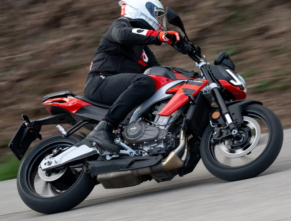 Une Aprilia 457 Tuono rouge, un motard habillé en noir, des gants rouges