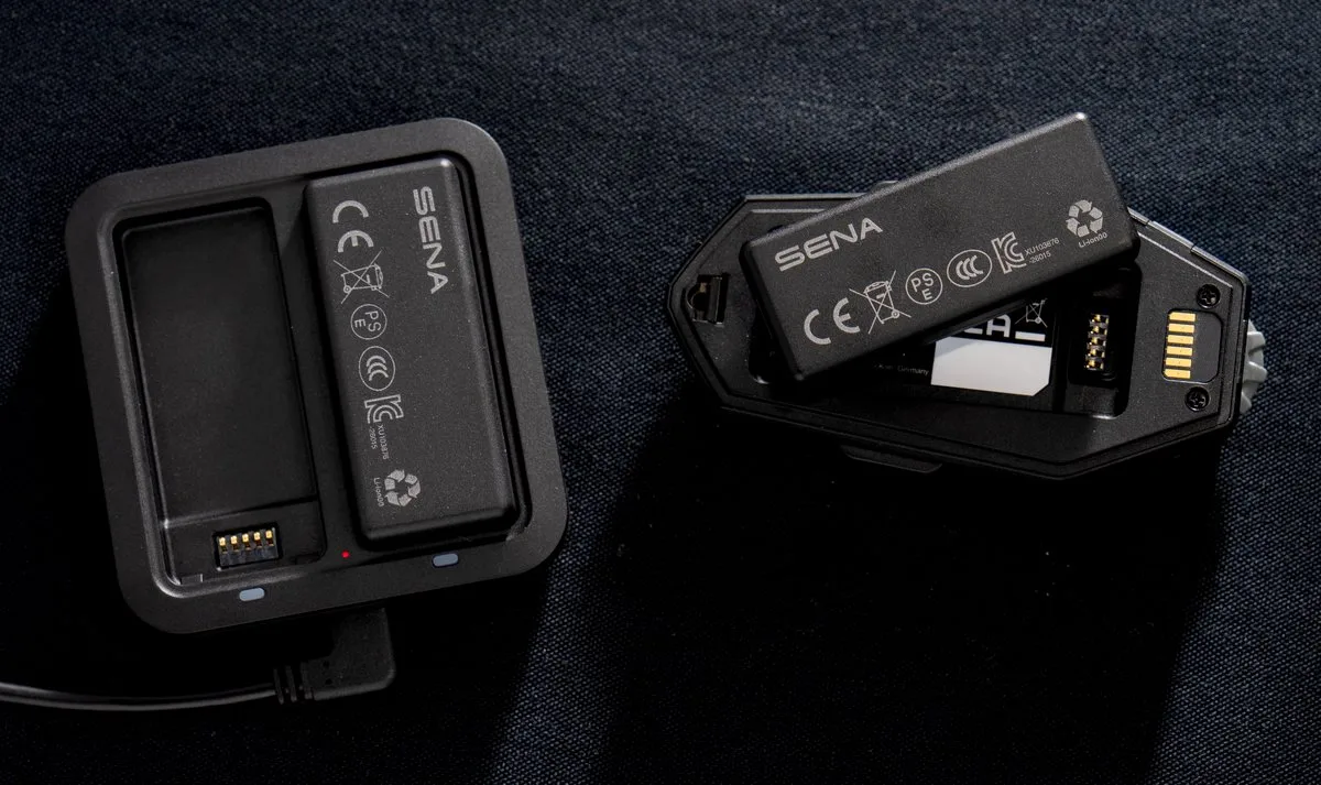 Un intercom Sena Apex, sa batterie et son chargeur sur fond noir