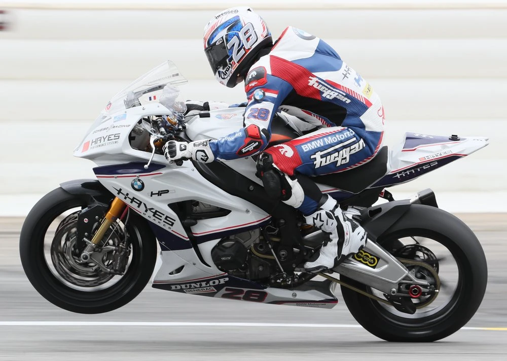 Une BMW S 1000 RR blanche en wheeling avec un pilote en combinaison bleu blanche et rouge