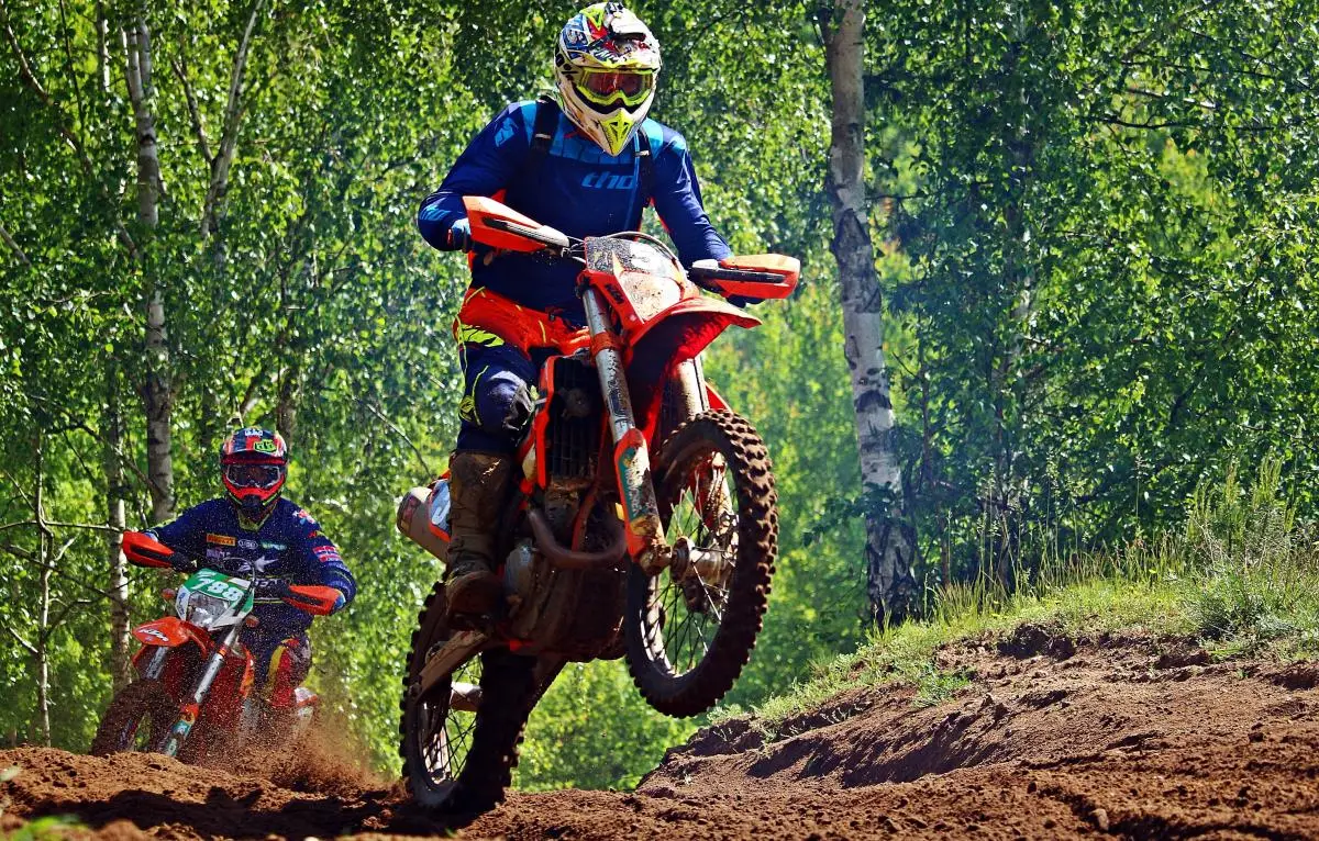deux motos d'enduro oranges, un chemin de terre, des arbres