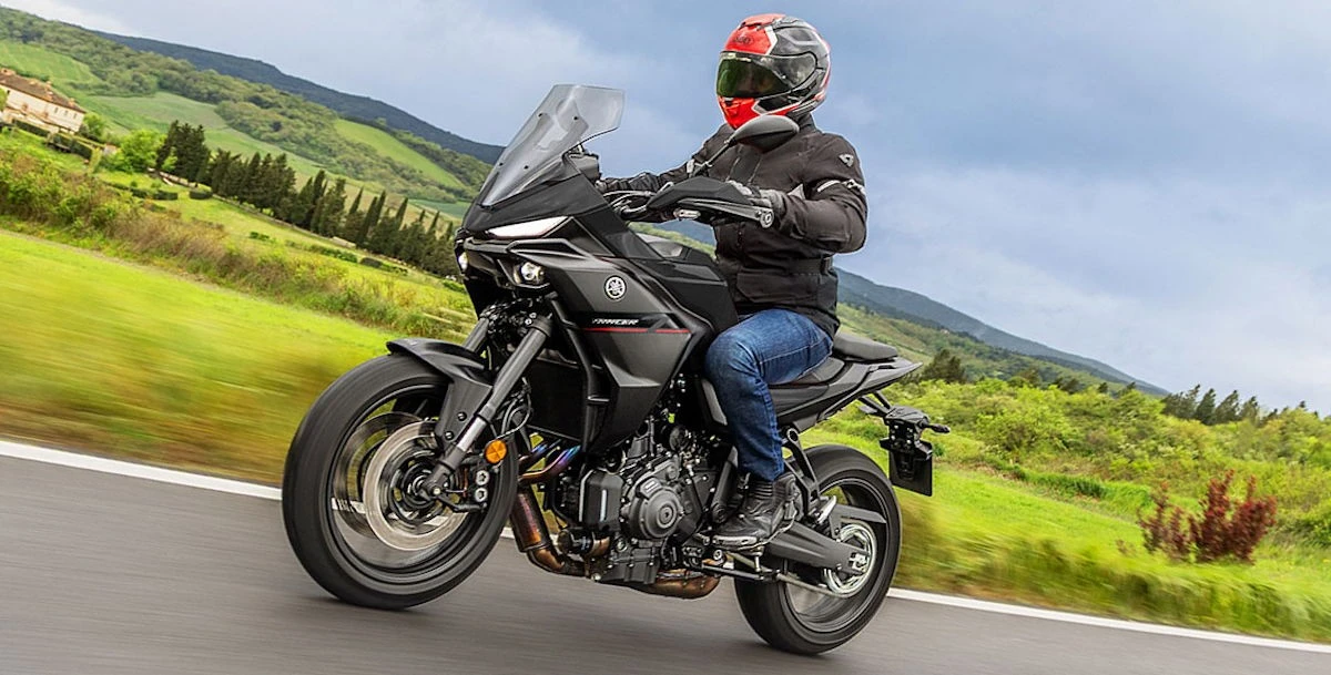 Une moto Yamaha Tracer 7 noire, une route, un paysage de campagne et un ciel nuageux