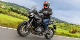 Une moto Yamaha Tracer 7 noire, une route, un paysage de campagne et un ciel nuageux