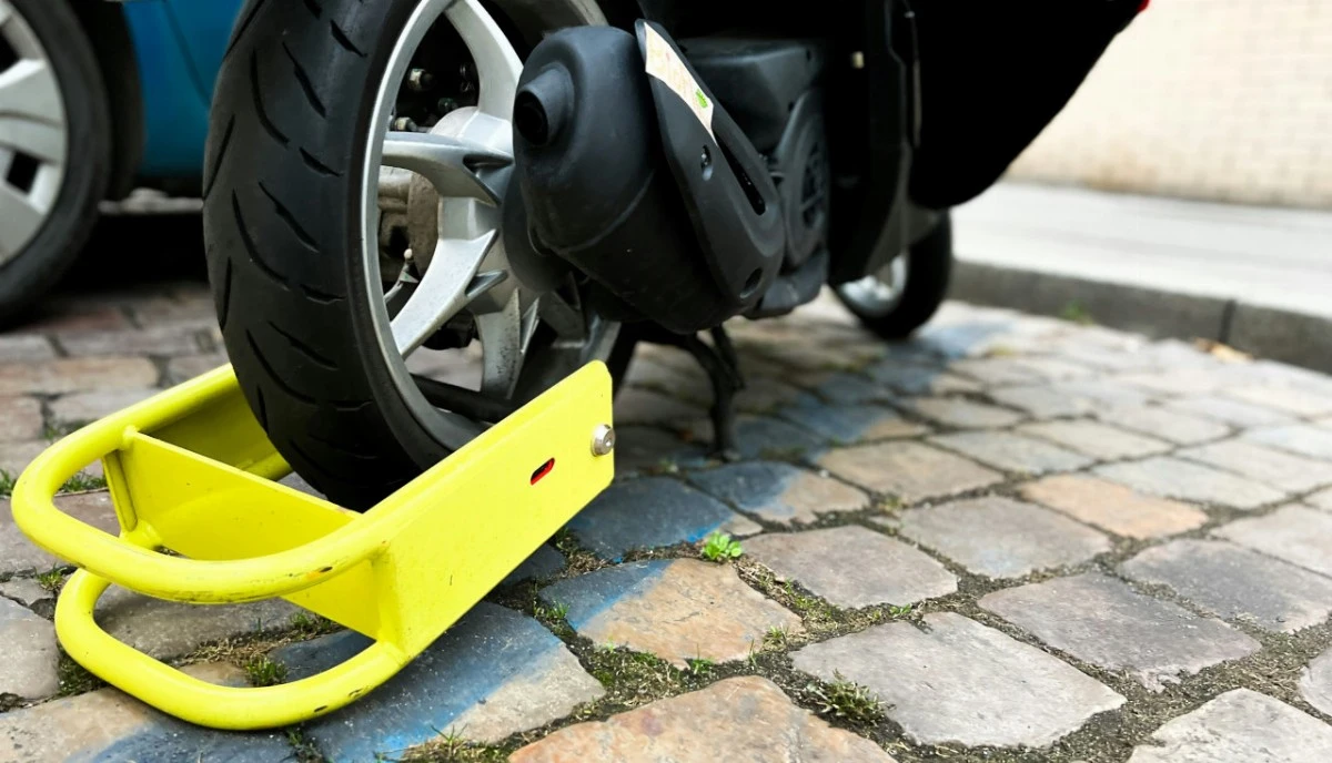 Un gros antivol jaune sur posé au sol et accroché à la roue arrière d'un scooter