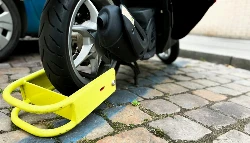 Un gros antivol jaune sur posé au sol et accroché à la roue arrière d'un scooter
