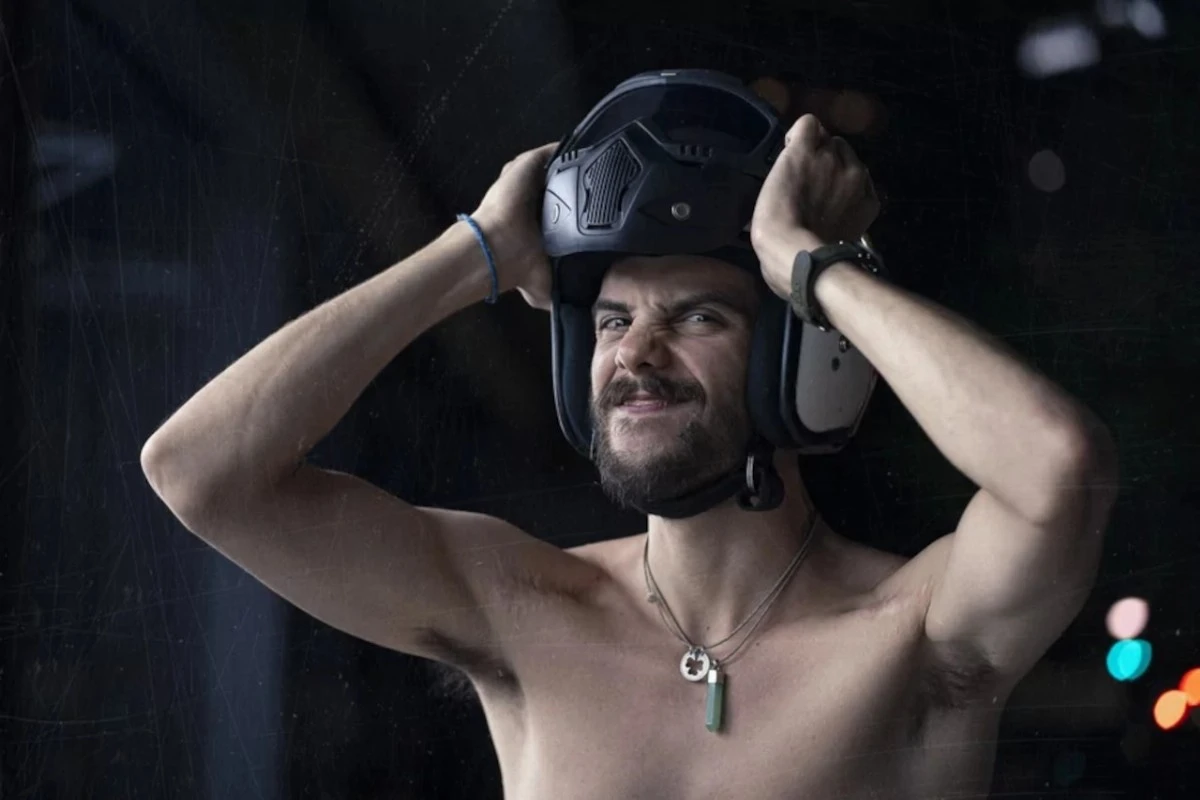 Un homme torse nu enfile un casque jet en faisant une grimace