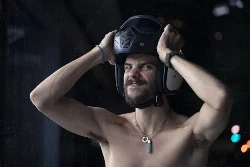 Un homme torse nu enfile un casque jet en faisant une grimace