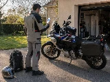Un motard de dos avec son téléphone et l'application partir léger, afin de préparer ses bagages pour un road trip moto de plusieurs jours. On voit sa BMW GS nettoyée et chargée avec ses sacoches cavalières.