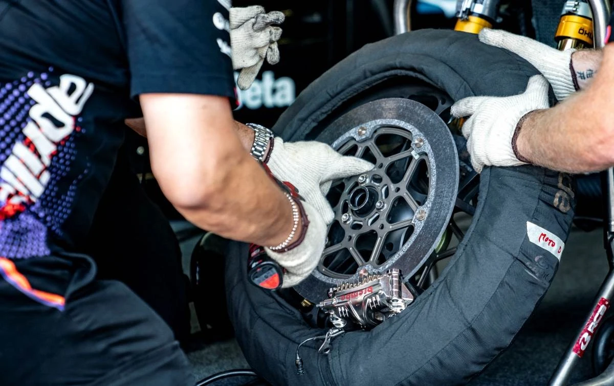 Un technicien manipulant une roue de moto avec un disque de frein en carbone et une couverture chauffante.