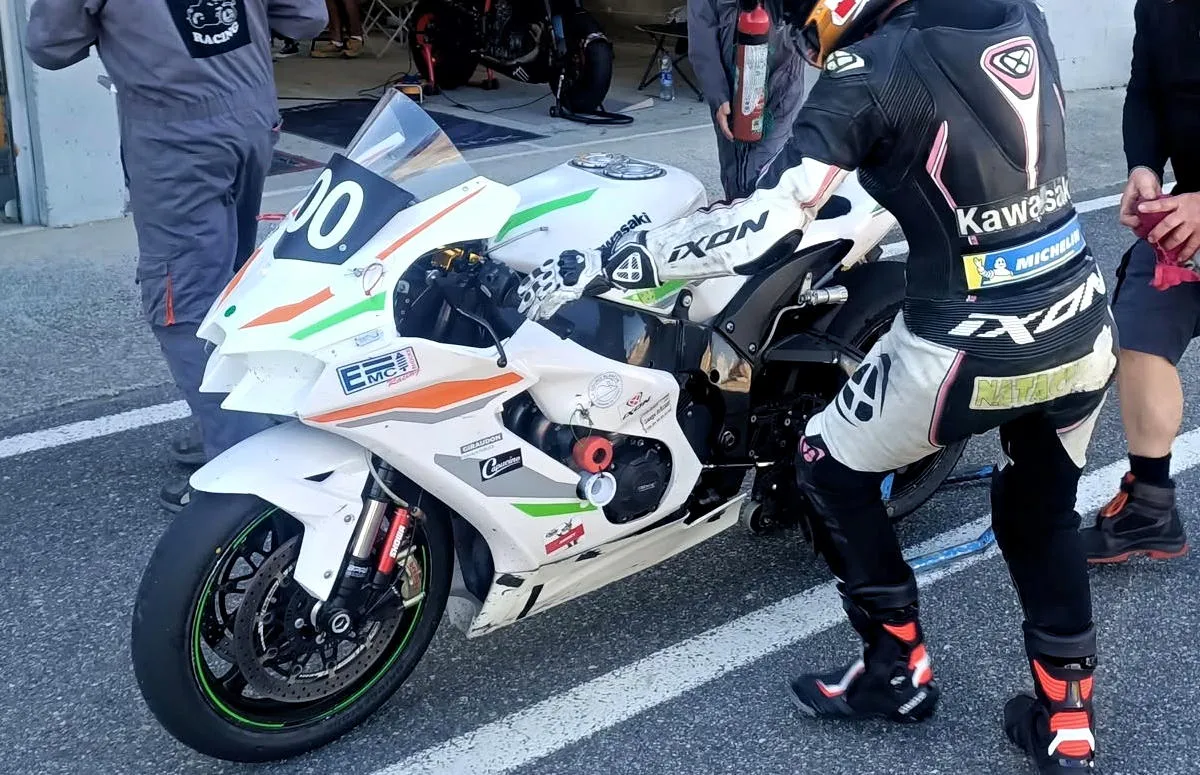 Une moto Kawasaki ZX-10R blanche et une pilote prête à monter dessus.