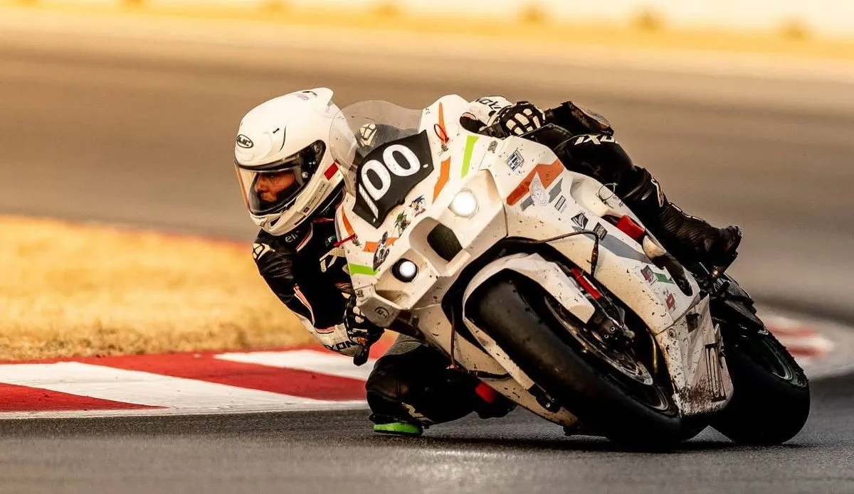 Une Kawasaki ZX-10R blanche avec le numéro 100 et une pilote en combinaison noire et blanche
