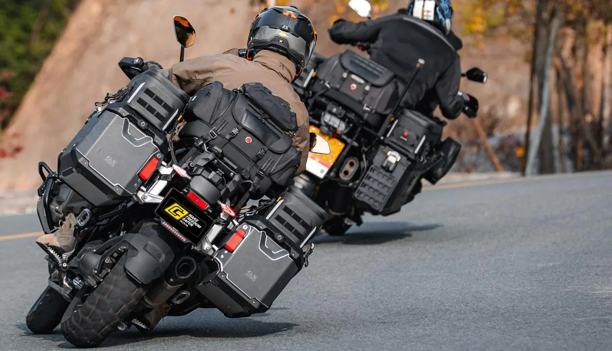 The rear of two motorcycles in a curve, with luggage