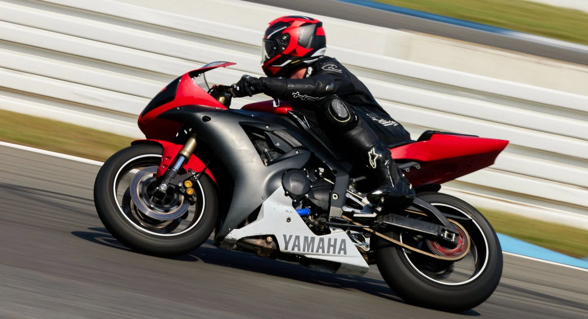 Une Yamaha YZF-R1 rouge noire et blanche sur circuit et un pilote avec un casque rouge et une combinaison noire.