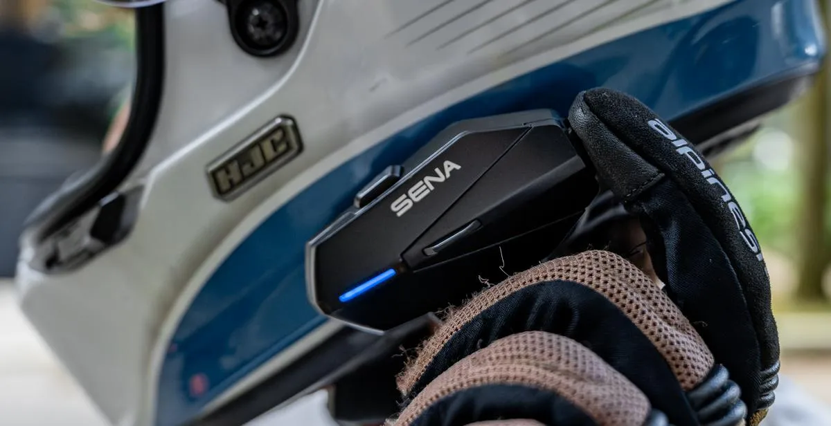 Un intercom Sena Apex, un gant de moto et un casque de moto blanc avec une bande bleu basse