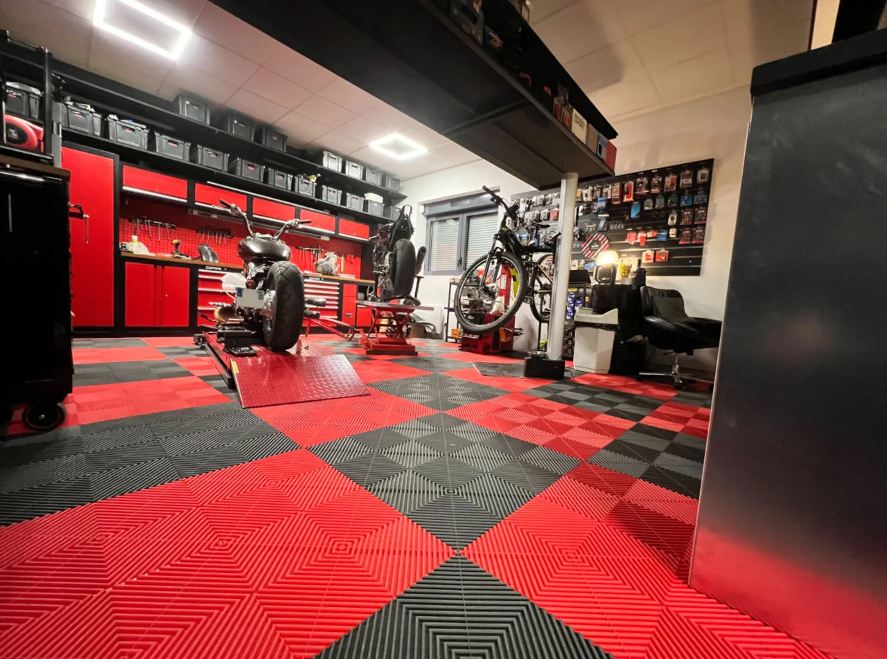 Un atelier moto et vélo avec des établis et coursives rouges et noires dans le fond, et des dalles rouges et noires au sol.