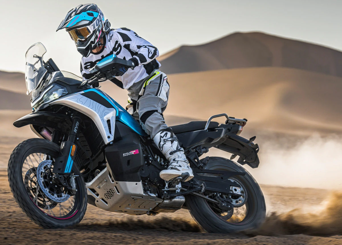 Motard au guidon du maxi-trail CFMOTO 1000 MT-X en plein dérapage dans le désert avec projection de sable.