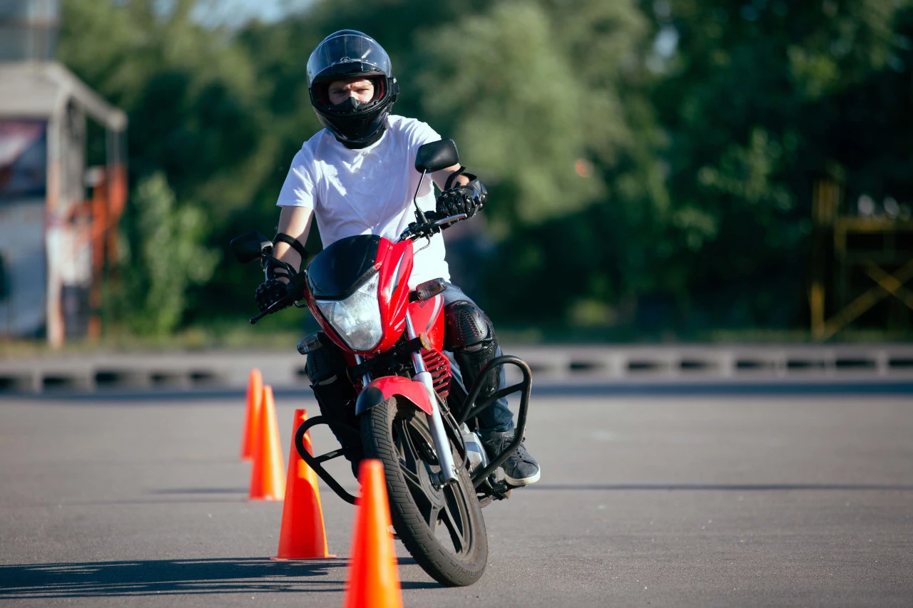 Un jeune motard apprend à manier une moto rouge entre des plots
