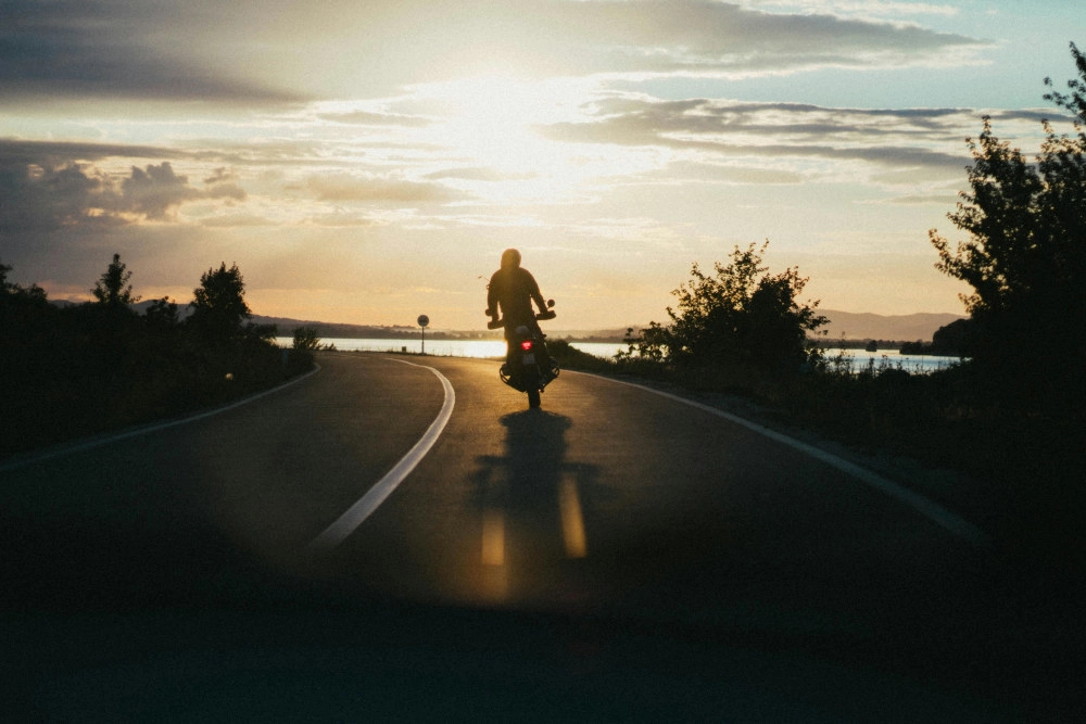 Une moto avec son pilote debout devant un couché de soleil