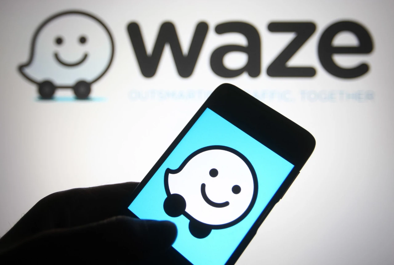 Une main avec un téléphone portable et l'application Waze qui se lance. En fond, on retrouve le logo de Waze