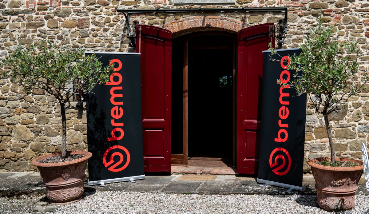 Une porte d'entrée de maison, deux arbres en pot et deux bannières Brembo